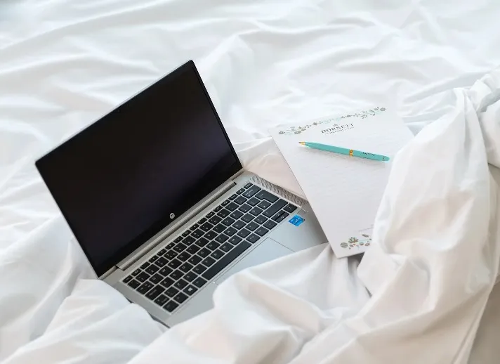 Laptop and dorsett writing pad and pen on a bed.