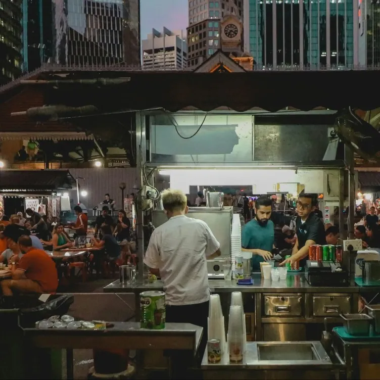 People ordering at the counter while a person preparing in a food cart