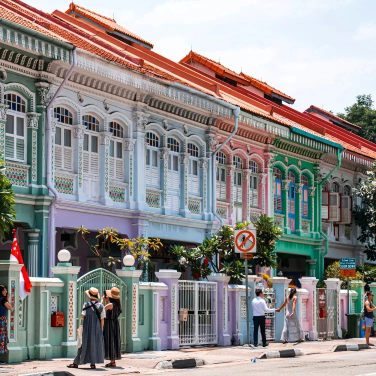 Pedestrians by colourful buildings while some are capturing photos.