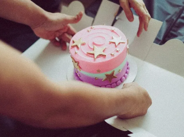 Two packing a pink, purple and green cake.