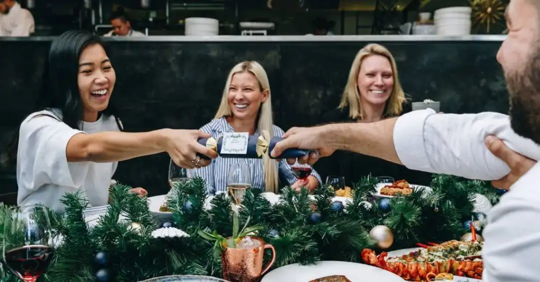 Friends gather at a restaurant Christmas lunch happily popping bon-bons