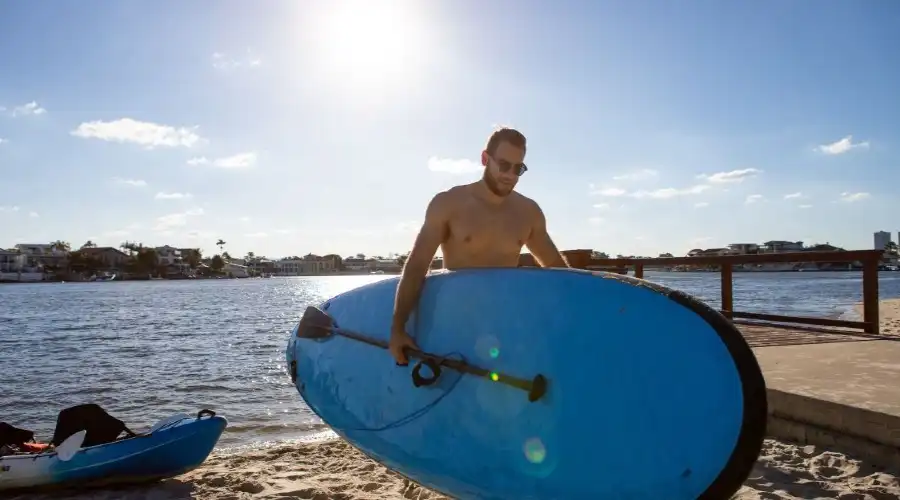 A man carries a blue stand up paddle board from the water
                                                                                                                                                                                                                                                                                                                                                                        Credit: Destination Gold Coast