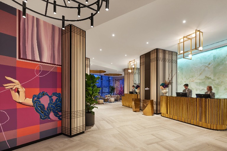 Image of a hotel lobby with two staff on the front desk and a big mural on the left