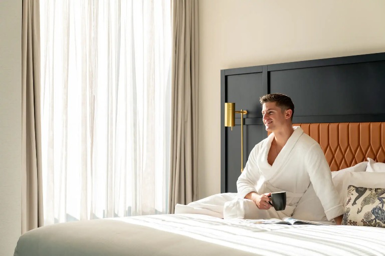 Man with a coffee on Dorsett Melbourne Balcony Suite bed