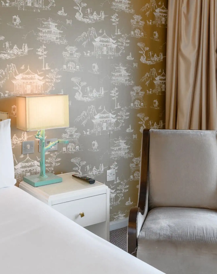 Grey cushioned armchair by white bedside table with night lamp.