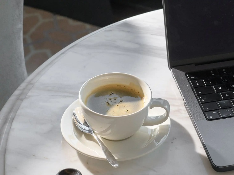 A cup of coffee next to a laptop on a white table.