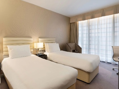 Twin beds and a working desk in the Deluxe Twin at Dorsett Shepherds Bush London Hotel