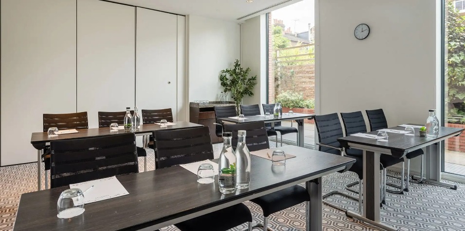 Four tables, each seating three people and a TV in the Heron Suite, West London.