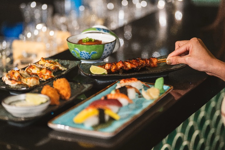 A woman grabbing a chicken skewer and other dishes on the table.