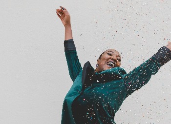 A woman wearing a green blazer smiling and celebrating with confetti.