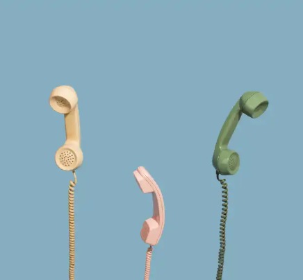 Green, pink and yellow coloured telephones on a blue background behind.