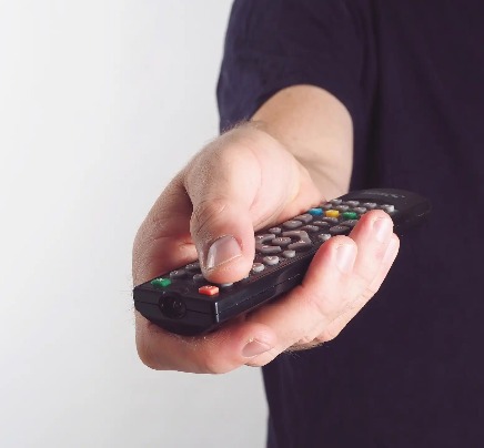 A man pressing a TV remote button.