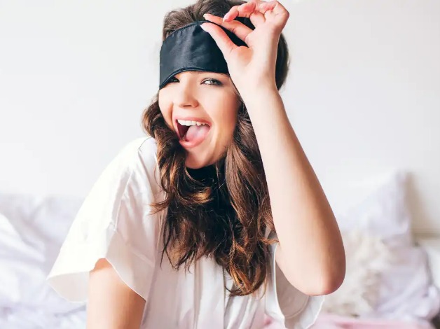 A girl wearing a baggy t-shirt and removing her sleep mask.