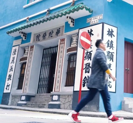 A man strolls the sidewalk in front of blue building on Wanchai Road