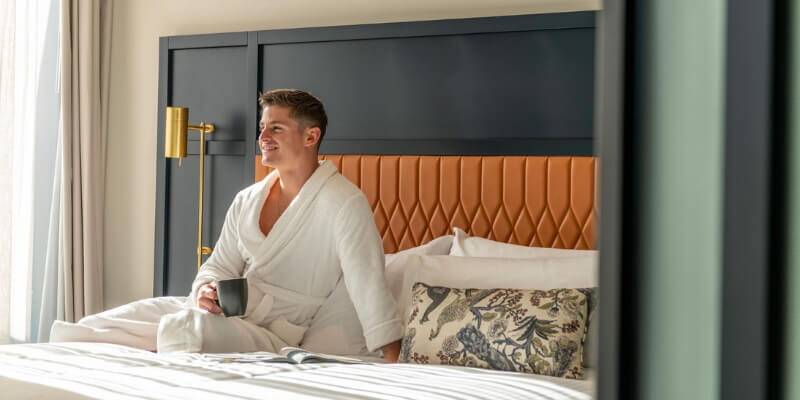 Dorsett guest in a white robe drinking coffee in bed