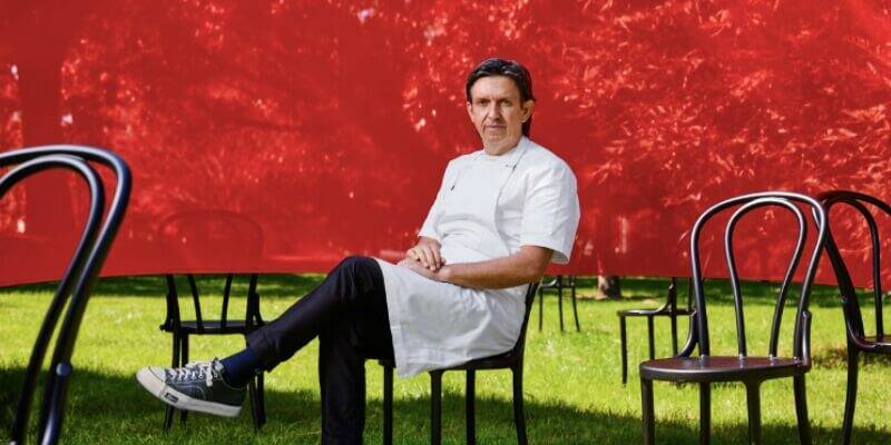 Chef Andrew McConnell sitting in front of a red backdrop